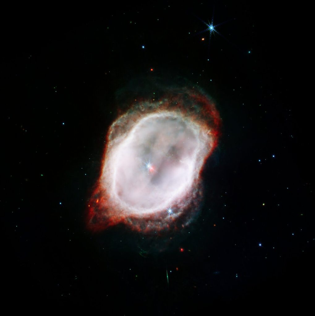 La vista de Webb de la Nebulosa del Anillo Sur aparece como un óvalo deforme que está ligeramente inclinado desde la parte superior izquierda hacia la parte inferior derecha. La imagen muestra dos estrellas que casi se superponen en el centro. Un gran óvalo blanco casi sólido rodea las estrellas centrales.